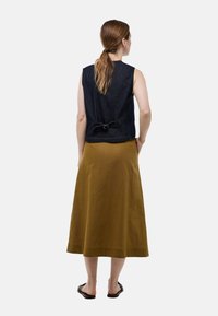 Top sans manches en denim avec un détail à nouer au dos, associé à une longue jupe moutarde. Les matériaux sont texturés, soulignant un style décontracté.