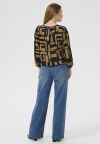 Black and tan patterned blouse with a round back neckline and gathered sleeves, paired with high-waisted, straight-leg blue jeans.