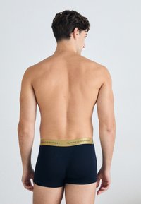 Marineblå boxer briefs med en gylden talje med "TOMMY HILFIGER" tekst. Blødt, tætsiddende design med en glat tekstur.