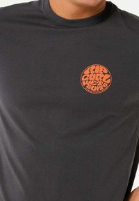 Graues langärmliges T-Shirt aus glattem Stoff, mit einem orangefarbenen runden Logo auf der linken Brust und stilisierter Schrift.