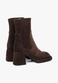 Hnědé nubukové kotníkové boty s robustním podpatkem, na zaoblenou špičku a prošitím podél horního okraje a bočních panelů.