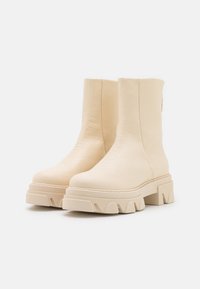 Beige Stiefeletten aus strukturiertem Leder, mit einer robusten Gummisohle mit Zickzackmuster und einem minimalistischen Design mit seitlicher Naht.