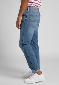 Vaaleansiniset farkut suoralla lahkeella, viisi taskua, kontrastiterssit ja hieman haalistumat, käytetty valkoisten lenkkareiden kanssa.