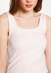 Camiseta sin mangas rosa hecha de tela suave. Presenta un escote redondeado y un pequeño logo blanco de Puma en el centro. Textura suave.