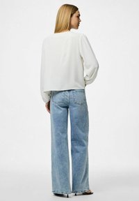 Weißes, gekürztes Oberteil mit Puffärmeln, kombiniert mit hellblauen, weit geschnittenen Jeans. Der Stoff wirkt strukturiert und leicht gerippt.