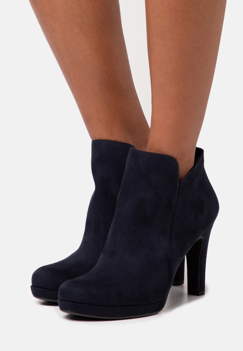 Bottines en daim bleu marine avec un bout rond, un talon aiguille haut et une texture lisse. Présente un design découpé au niveau de la cheville.