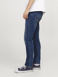 Jeans din denim indigo cu croială slim, dotate cu cinci buzunare, cusături subtile și adidași uzați albi cu accente negre.