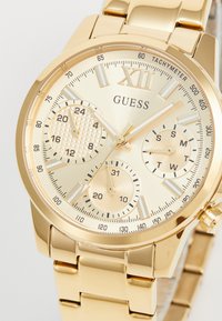 Guld rustfrit stål ur med en struktureret guldskive, tre subskiver og et poleret armbånd. Markeringer inkluderer tal og tachymeter.