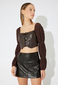Brun læder cropped top med puffede teksturerede ærmer og snørebånd foran. Kombinationen med en sort skinnende mini nederdel.