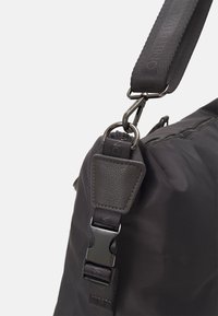 Détail d'un sac en nylon noir montrant une sangle réglable, des métaux, des accents en cuir et une surface texturée. Comprend un clip et des points d'attache robustes.