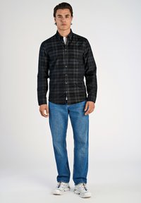 Zwart en grijs geruite overhemden in een katoenmix, gecombineerd met blauwe jeans en witte sneakers. Effen achtergrond.