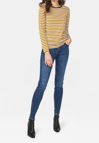 Randig långärmad topp i senapsgul och vit med svarta kanter, matchad med mörkblå jeans i skinny-modell och svarta ankelskor.