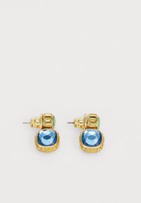 Boucles d'oreilles dorées présentant une grande pierre bleue facettée encadrée d'une monture texturée, accentuées par un haut décoratif vert et or.