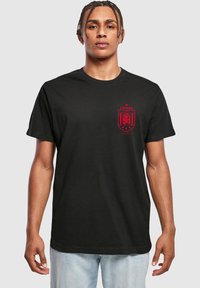 Tricou din bumbac negru cu un emblema roșie a Spaniei pe partea stângă a pieptului, cu un gât clasic rotund și mâneci scurte.