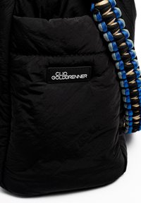 Black nylon bag with a textured surface, featuring a logo patch and a braided strap in blue, gray, and black hues.