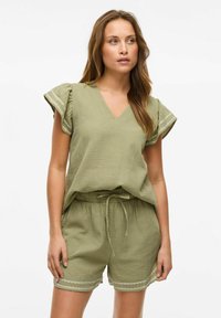 Conjunto de ropa de casa en verde oliva que presenta una blusa de escote en V con mangas acampanadas y pantalones cortos a juego con cordón y ribete decorativo.