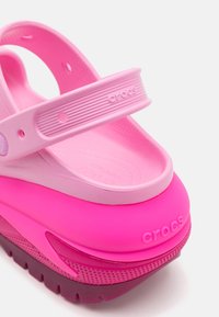Crocs roz cu un design stratificat. Include o curea roz deschis și o talpă roz îndrăzneață cu o suprafață texturată. Logo-ul "Crocs" pe lateral.