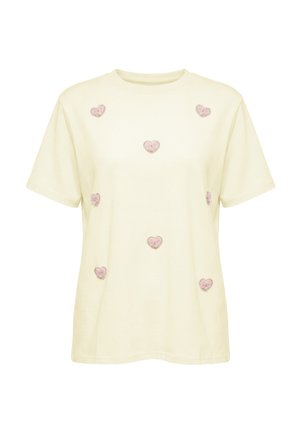 Kremowy t-shirt z krótkim rękawem z siedmioma różowymi, haftowanymi naszywkami w kształcie serca równomiernie rozmieszczonymi z przodu. Brak widocznych logo lub tekstu.