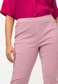 Rosa und weiße gestreifte Hose mit elastischem Bund, schlanker Schnitt und glatter Textur. Eine Hand des Models ist auf der Hüfte positioniert.