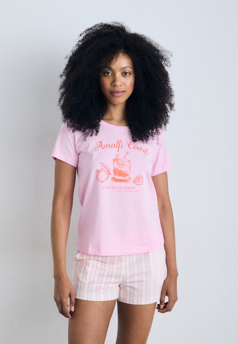 T-shirt de algodão rosa claro com a inscrição "Costa Amalfitana" e um gráfico de cocktail em laranja. Combinado com calções brancos com riscas verticais em vermelho e rosa.