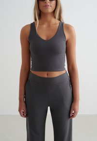 Szary krótki top z dekoltem w serek i szerokimi ramiączkami, zestawiony z pasującymi wysokim stanem spodniami. Tkanina wygląda na gładką i elastyczną.