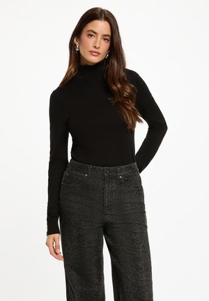 Pull à col roulé noir associé à un jean taille haute en imprimé serpent noir. Texture lisse avec des manches longues et une conception ajustée.