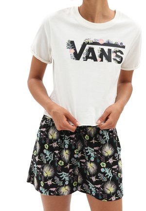 Biały krótki T-shirt z czarnym logo Vans ozdobiony różowymi kwiatami, zestawiony z czarnymi kwiatowymi szortami z pastelowo zielonymi i żółtymi liśćmi.