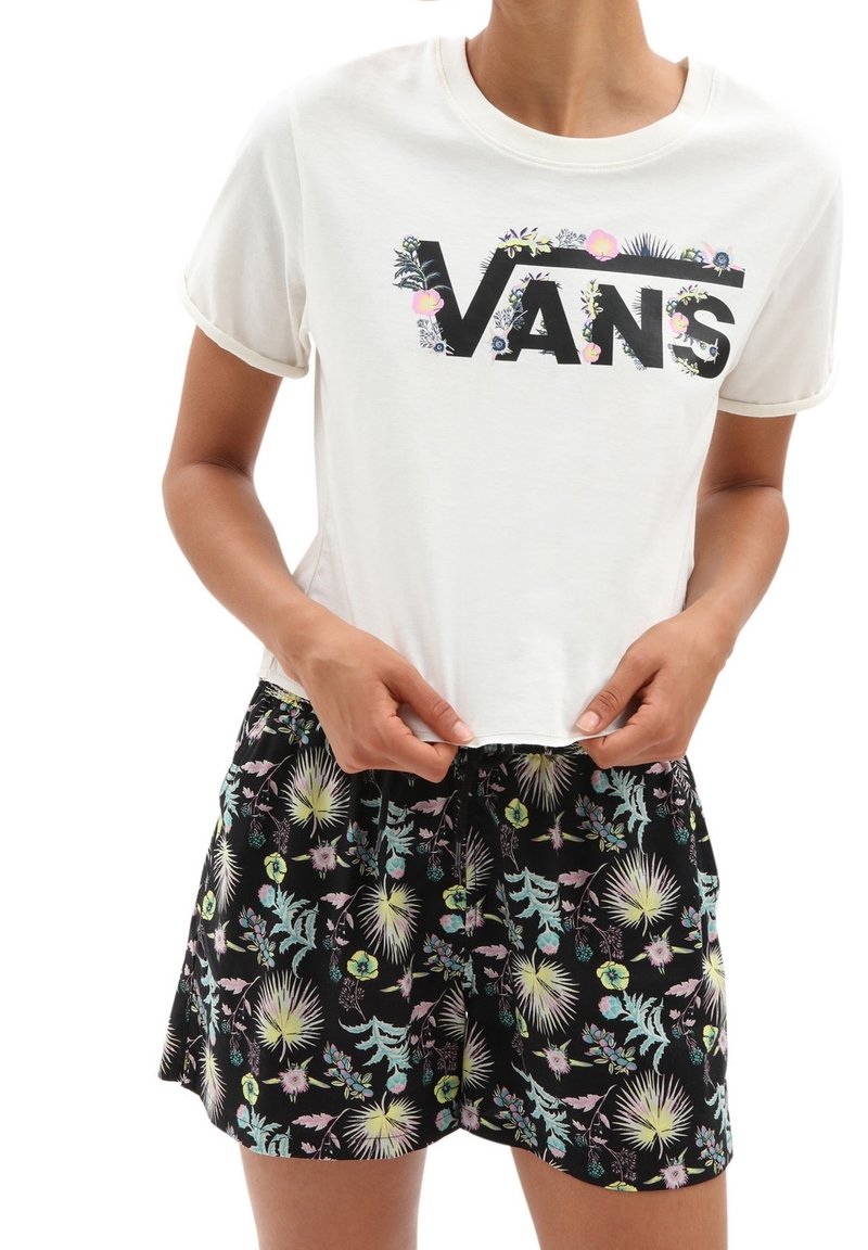 T-shirt court blanc avec logo Vans noir décoré de fleurs roses, assorti à un short noir à motifs floraux avec des feuilles vert pastel et jaune.
