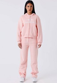 Roze zip-up hoodie met een logo, gecombineerd met bijpassende sweatpants. Zachte stof, ontspannen pasvorm, geribbelde cuffs en tailleband voor comfort.