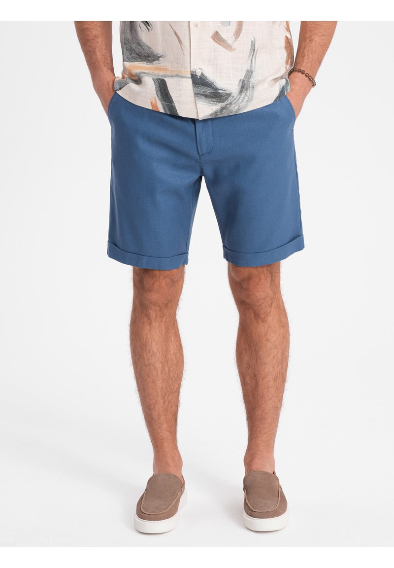 Shorts bleus en tissu léger, présentant une coupe droite, une ourlet retroussé et des poches latérales, associés à des chaussures marron à enfiler.