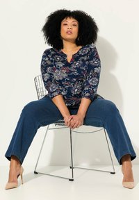 Marinebluse mit floraler Optik und Dreiviertelärmeln, V-Ausschnitt, kombiniert mit dunkelblauen weiten Jeans und beigen spitzen Absatzschuhen.