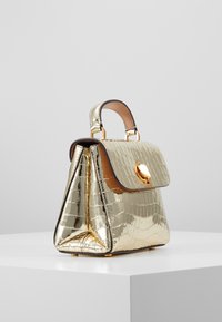 Złota torebka z lakierowanej skóry z teksturą w kształcie krokodylej skóry, o kwadratowym kształcie, z krótkim uchwytem i złotym zapięciem na przedniej klapie.