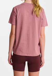 Rosa Baumwoll-T-Shirt mit kurzen Ärmeln, Rundhalsausschnitt und lässiger Passform, kombiniert mit kastanienbraunen enganliegenden Shorts. Glatte Textur, einfaches Design.