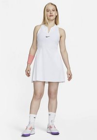 Valge varrukateta tennisekleit kõrge kaelusega ja musta Nike logoga. Käel kantakse roosat randmeriba ning jalas on valged tossud lillade detailidega.