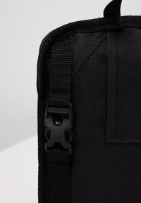 Czarna torba z tkaniny o gładkiej fakturze, regulowanym paskiem oraz solidnym plastikowym zatrzaskiem zapewniającym pewne zapięcie.