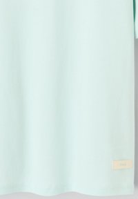 Tissu bleu-vert clair avec une petite étiquette rectangulaire beige cousue près du bord inférieur du côté droit.