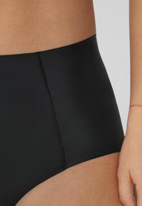 Hochgeschnittene schwarze Unterwäsche aus glattem Stoff mit nahtlosem Design und subtilen Nähten entlang der Kanten für Komfort und Unterstützung.