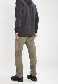 Donkergrijze hoodie met lange mouwen, gecombineerd met olijfgroene cargobroek met zakken en zwarte enkellaarsjes.