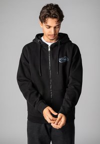 Black zip-up hoodie made from cotton blend fabric, featuring a front pocket, drawstrings, and a blue logo design on the chest.