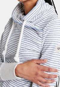 Sudadera a rayas en azul claro y blanco, con cuello tipo cowl y cordones, textura suave y puños acanalados; detalle del logo en la manga.