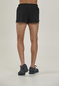 Sorte træningsshorts med elastisk talje, over-knæ længde, parret med grå løbesko med strukturerede såler og snører.