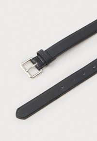 Crni kožni pojas sa srebrnom pravokutnom kopčom i brojnim rupama za podešavanje, položen ravno na svijetloj pozadini.