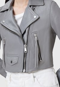 Giubbotto da moto cropped in pelle grigia con colletto a revers, accessori in argento, zip asimmetriche e dettagli delle tasche frontali.