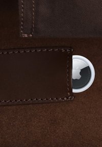 Apple AirTag partiellement visible à l'intérieur d'une poche de portefeuille en cuir marron avec une doublure en tissu foncé au-dessus.