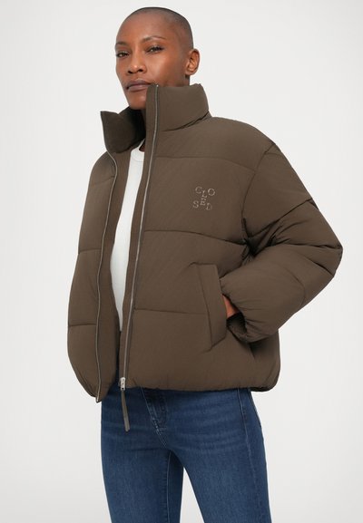Giacca imbottita marrone con colletto alto, chiusura a zip e logo sul petto. Dispone di due tasche anteriori e di una texture elegante e morbida.