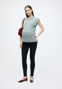 Sivý rebrovaný pletený top s krátkymi rukávmi, detailmi so gombíkmi na boku, v kombinácii s čiernymi legínami a lesklými červenými balerínkami. Červená kabelka cez rameno.