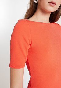 Kortärmad blus i stark orange, med en texturerad tyg och en fyrkantig halsringning som betonar en skräddarsydd passform.