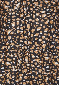 Textilie s černým pozadím a nepravidelným leopardím vzorem v béžové a bílé barvě.