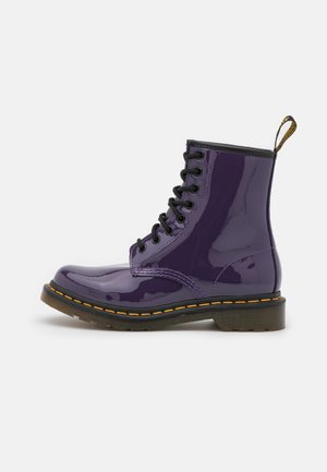Bottine en cuir verni violet avec lacets noirs, couture jaune et languette à l'arrière. Finition brillante, bout arrondi et semelle robuste.