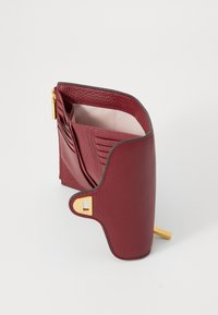 Portafoglio in pelle borgogna con finitura testurizzata. Presenta una cerniera dorata, slot per carte e un design pieghevole. L'interno è di colore chiaro.